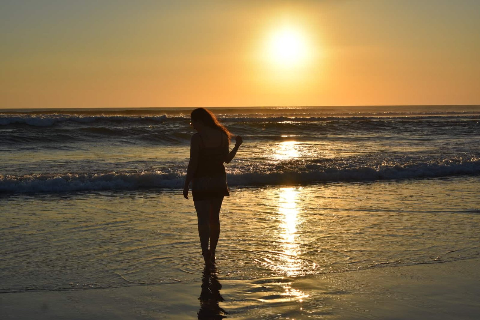 Solo female traveller admiring a stunning golden sunset at the beach in Bali, Indonesia.