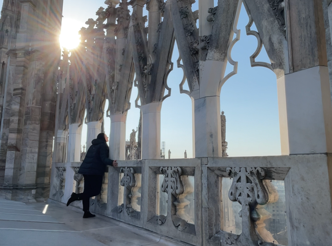Against the backdrop of a sinking sun, capture the essence of budget-friendly adventure while Travelling on a shoestring budget. The distant figure stands atop the majestic Duomo di Milano, a testament to the art of exploring more with less